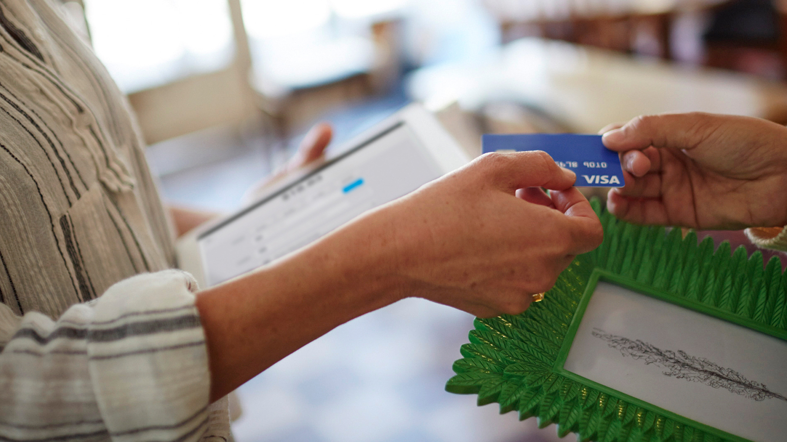Man handing Visa card to female retailer for purchase.