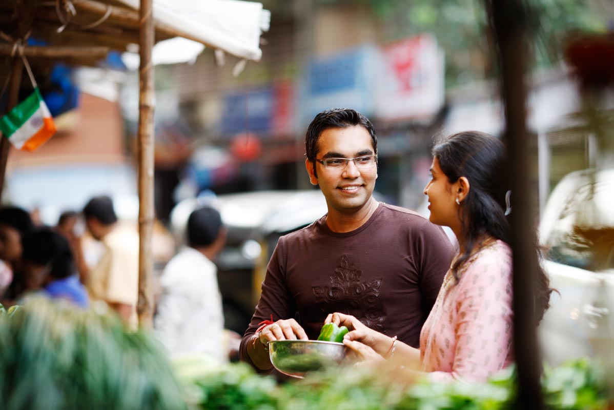 Indian man and woman talking at a vegetable stand in an outdoor market. 