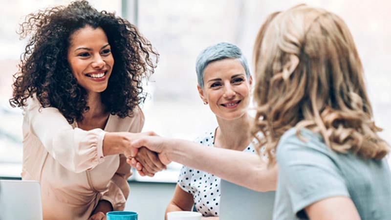 Three business casual women shaking hands at office.